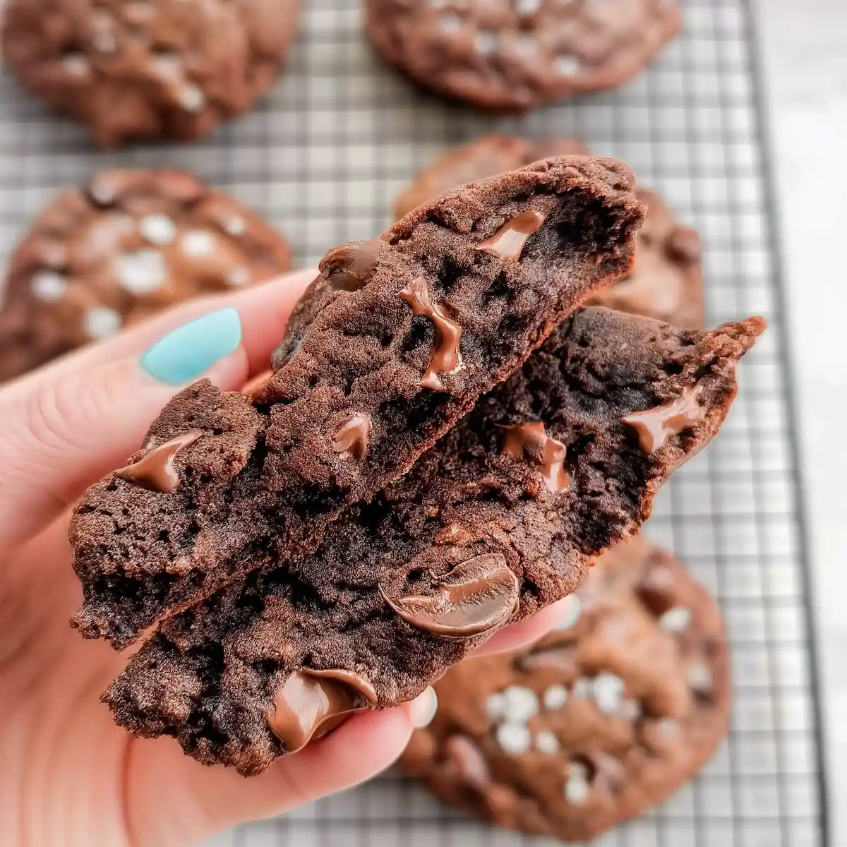gluten-free-crumbl-dark-dream-cookie-fudgy-center A hand holding a gluten free Crumbl Dark Dream cookie split in half, revealing a rich, fudgy interior with melted chocolate chips