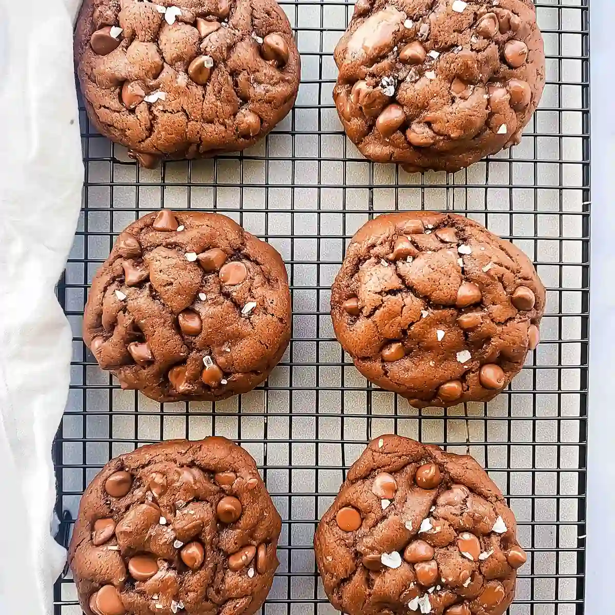 gluten-free-crumbl-dark-dream-cookies-wire-rack Six gluten free Crumbl Dark Dream cookies on a wire rack, packed with chocolate chips and topped with flaky sea salt