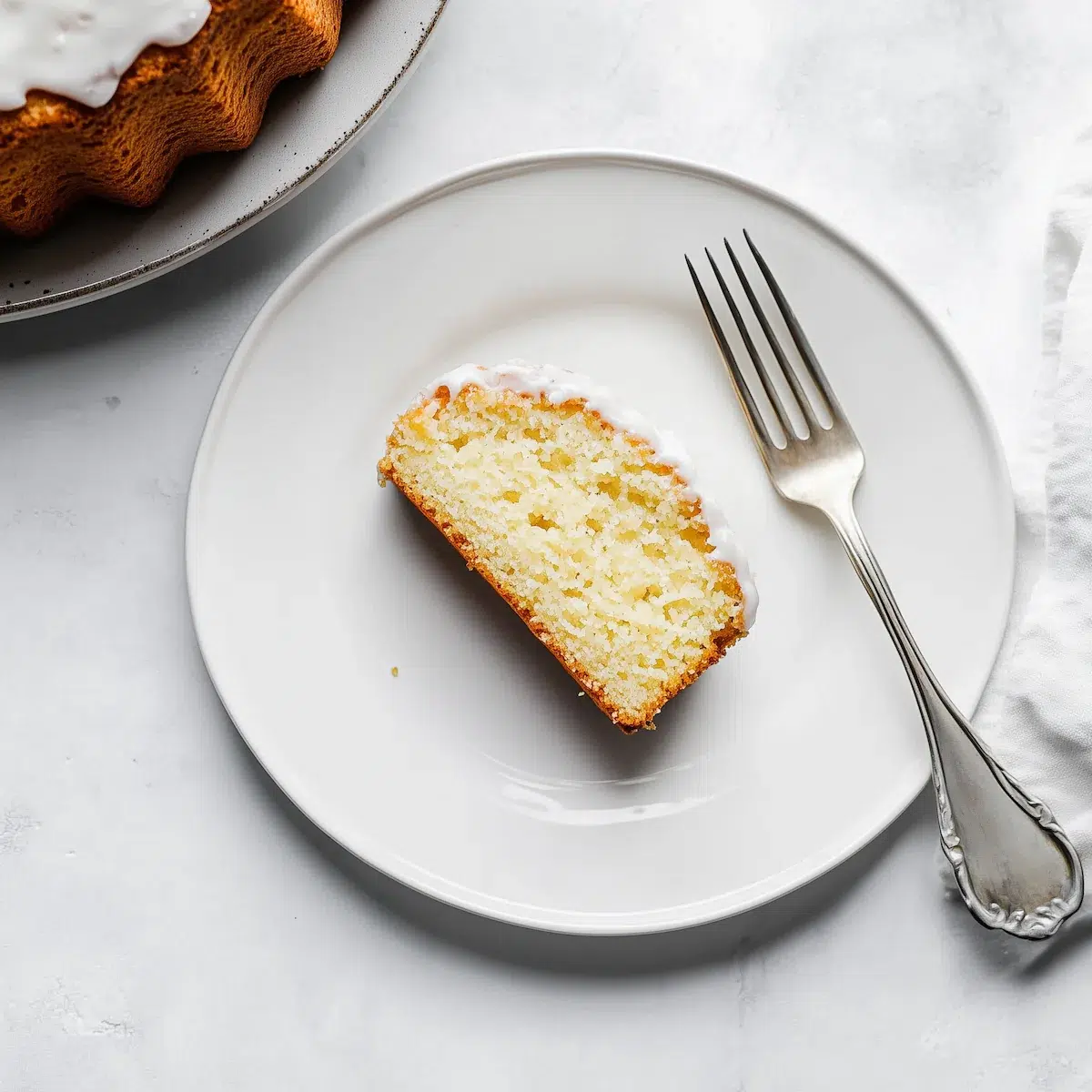 sliced-gluten-free-lemon-bundt-cake-with-glaze-recipe A single slice of gluten-free lemon bundt cake with lemon glaze on a white plate with a fork